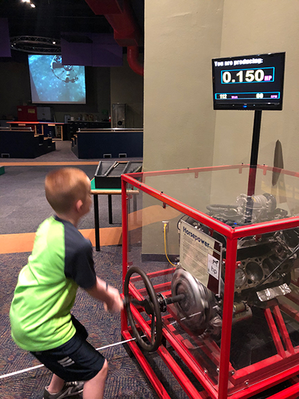 A boy works with a machine to measure horsepower at a science museum.